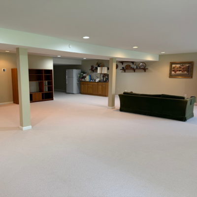 Finished basement with light carpet, a green sofa, bookshelves, and built-in storage after carpet installation in Allentown, PA.